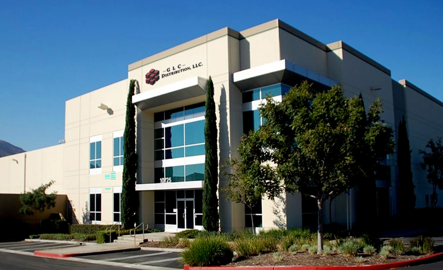 Exterior of the GLC Distribution facility with company signage, glass entrance, landscaped grounds, and a clear blue sky.