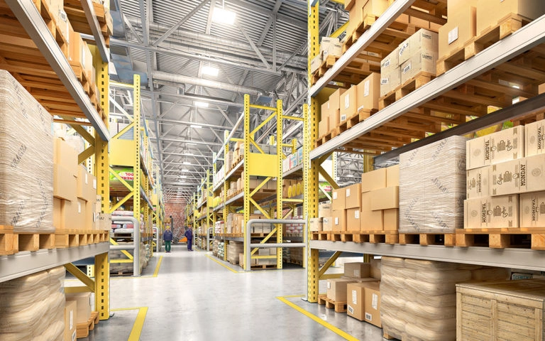 Warehousing and Distribution Operations Modern distribution warehouse with tall pallet racks filled with boxed and shrink-wrapped inventory along a wide, organized aisle.