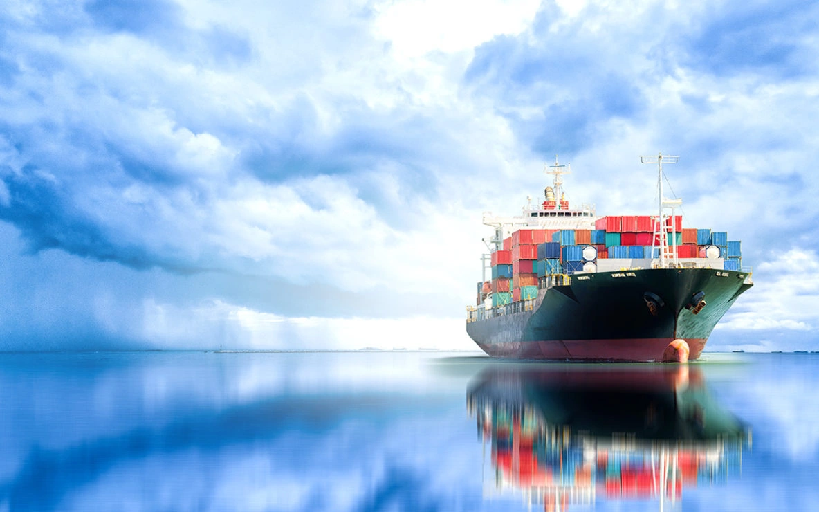 International Ocean Freight Shipping Services Container ship carrying multicolored cargo containers across calm ocean waters beneath a dramatic blue sky.